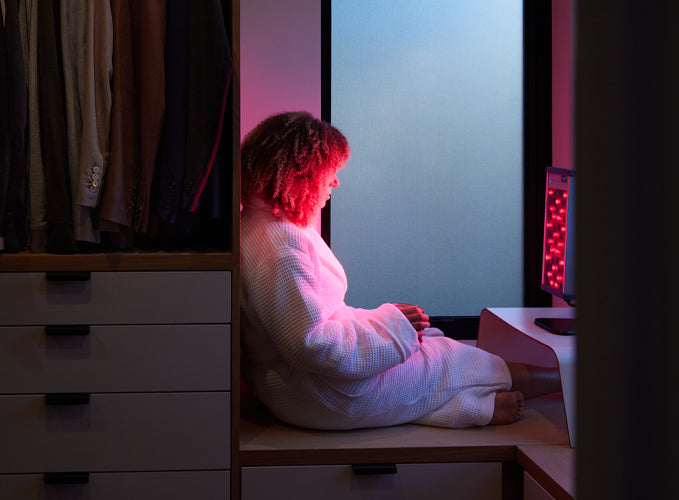 Woman sitting in front of a red light device in her robe