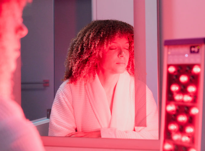 Woman with eyes closed sitting in front of red light device with face illuminated